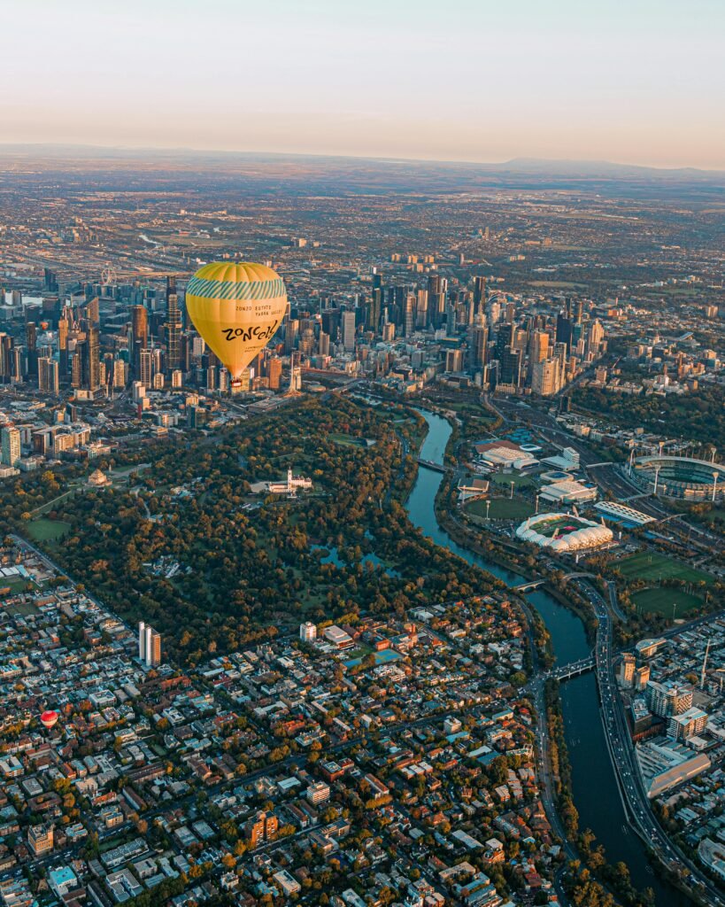 Dramatic aerial shot of a hot air balloon over Melbourne's skyline at sunrise.