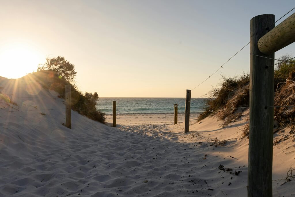 Tranquil pathway leading to Cottesloe Beach at sunset with soft sand and ocean view.