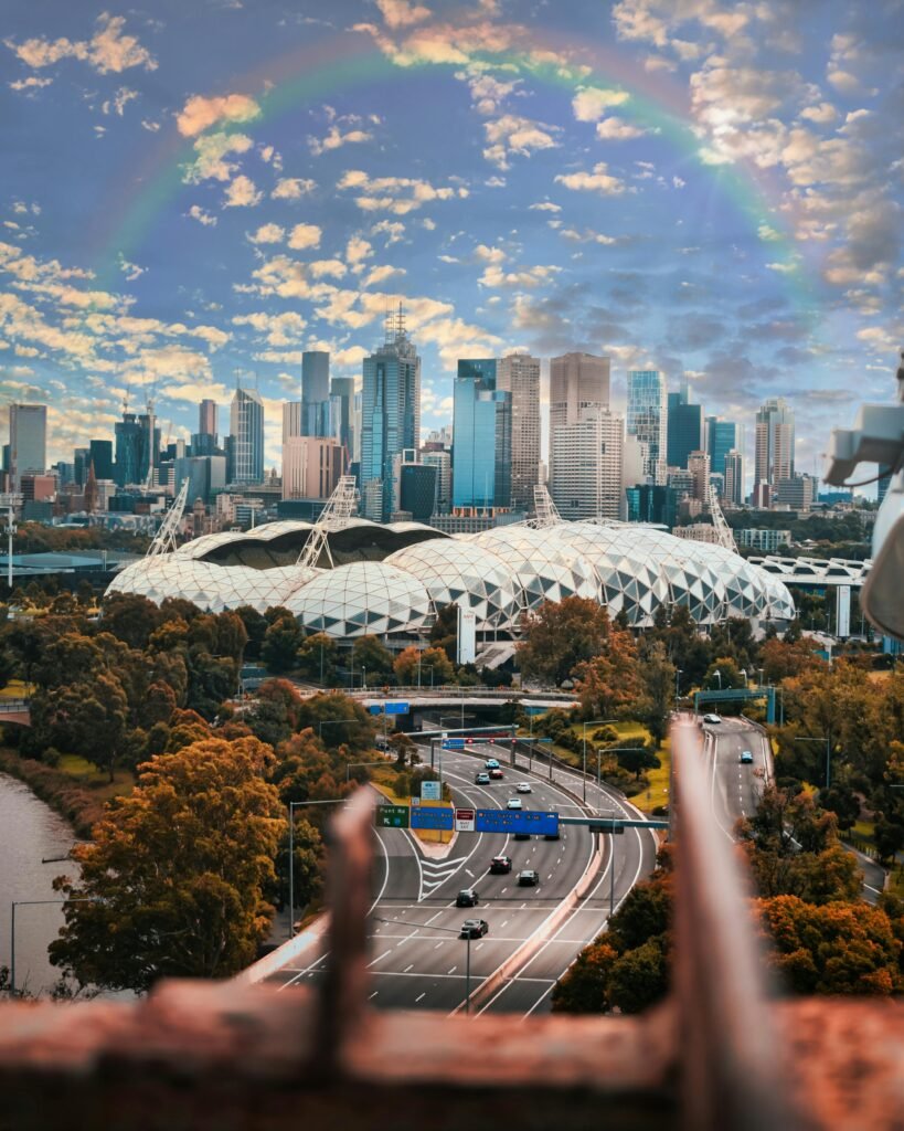 A stunning view of Melbourne's skyline, showcasing buildings and AAMI stadium under a rainbow.